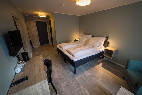 Habitación de hotel con cama, escritorio, silla, televisor y puerta.