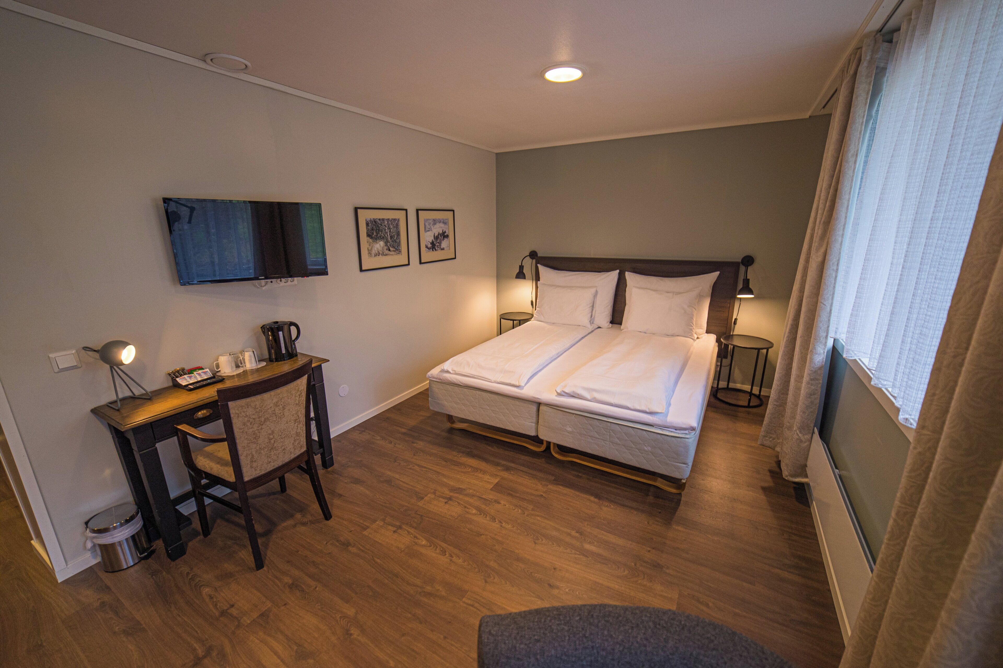 Una habitación de hotel con una cama, un escritorio con silla, televisión y una ventana con cortinas.