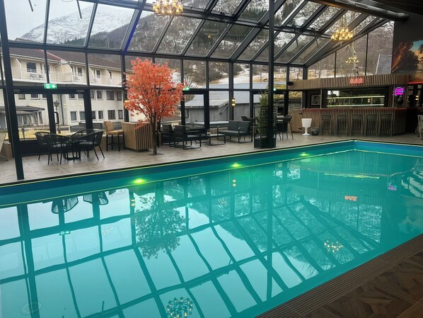 Una piscina interior con paredes de vidrio, zona de bar y asientos.