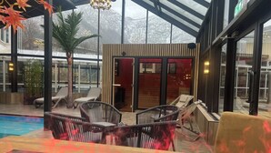 Un salon vitré avec une piscine, des meubles en osier et une vue sur une montagne enneigée.