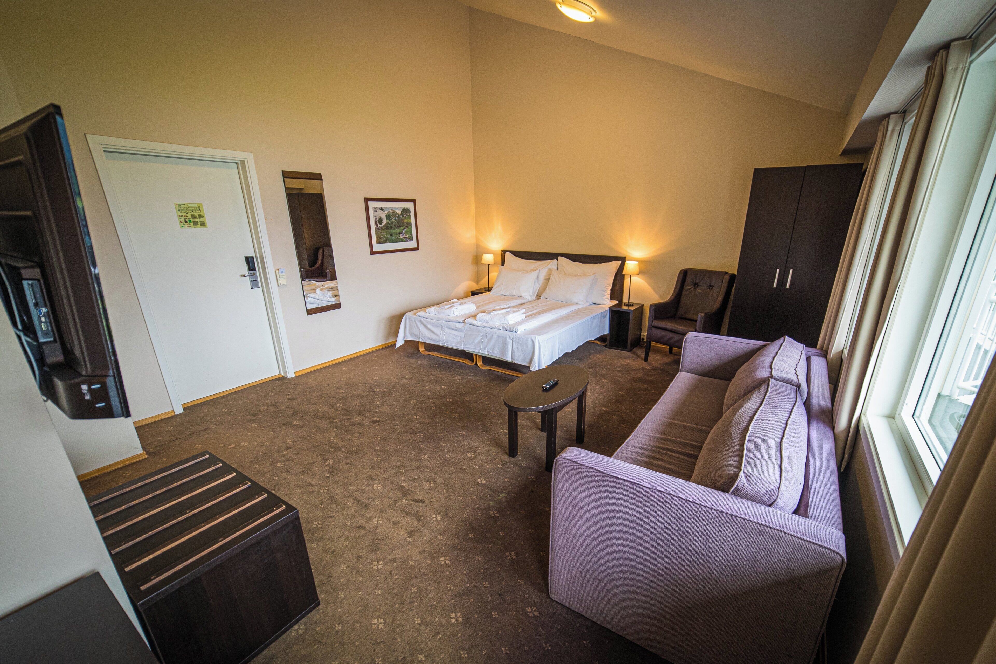 Une chambre d’hôtel avec un lit, un canapé, une petite table, une armoire et une porte.