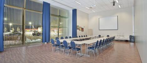 A conference room with a long table, chairs, a projector screen, and a large window with blinds.