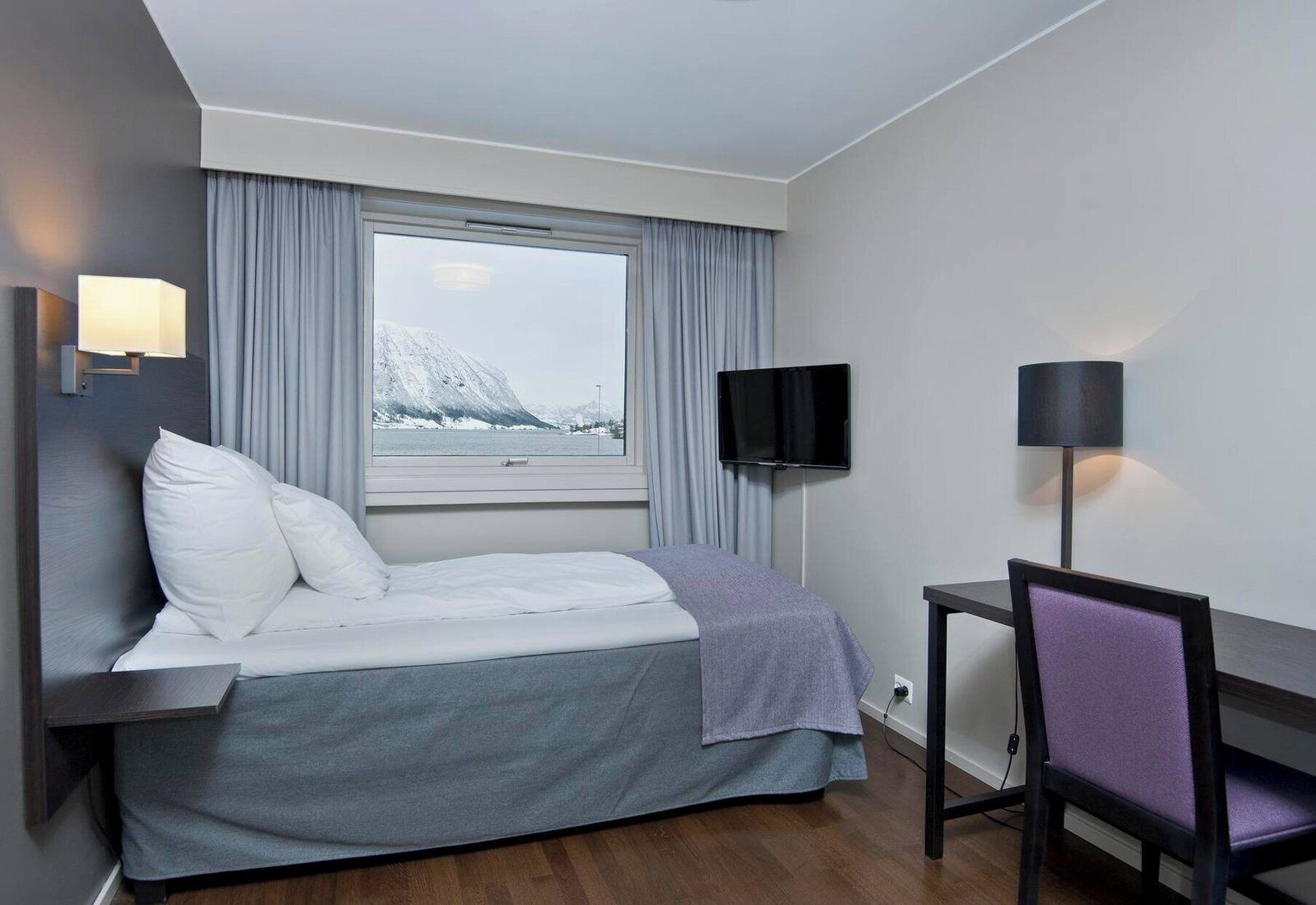 Une chambre d’hôtel avec un lit, une télévision, un bureau et une fenêtre donnant sur un paysage enneigé.