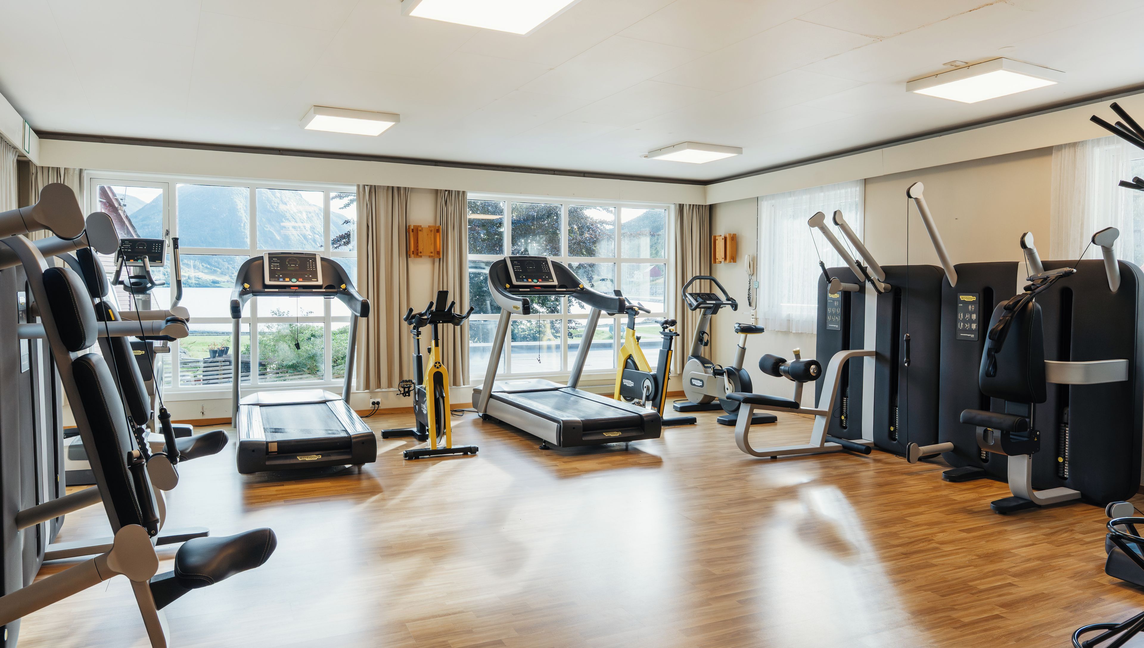 A gym with cardio machines, weight training equipment, and large windows offering a view of the outdoors.