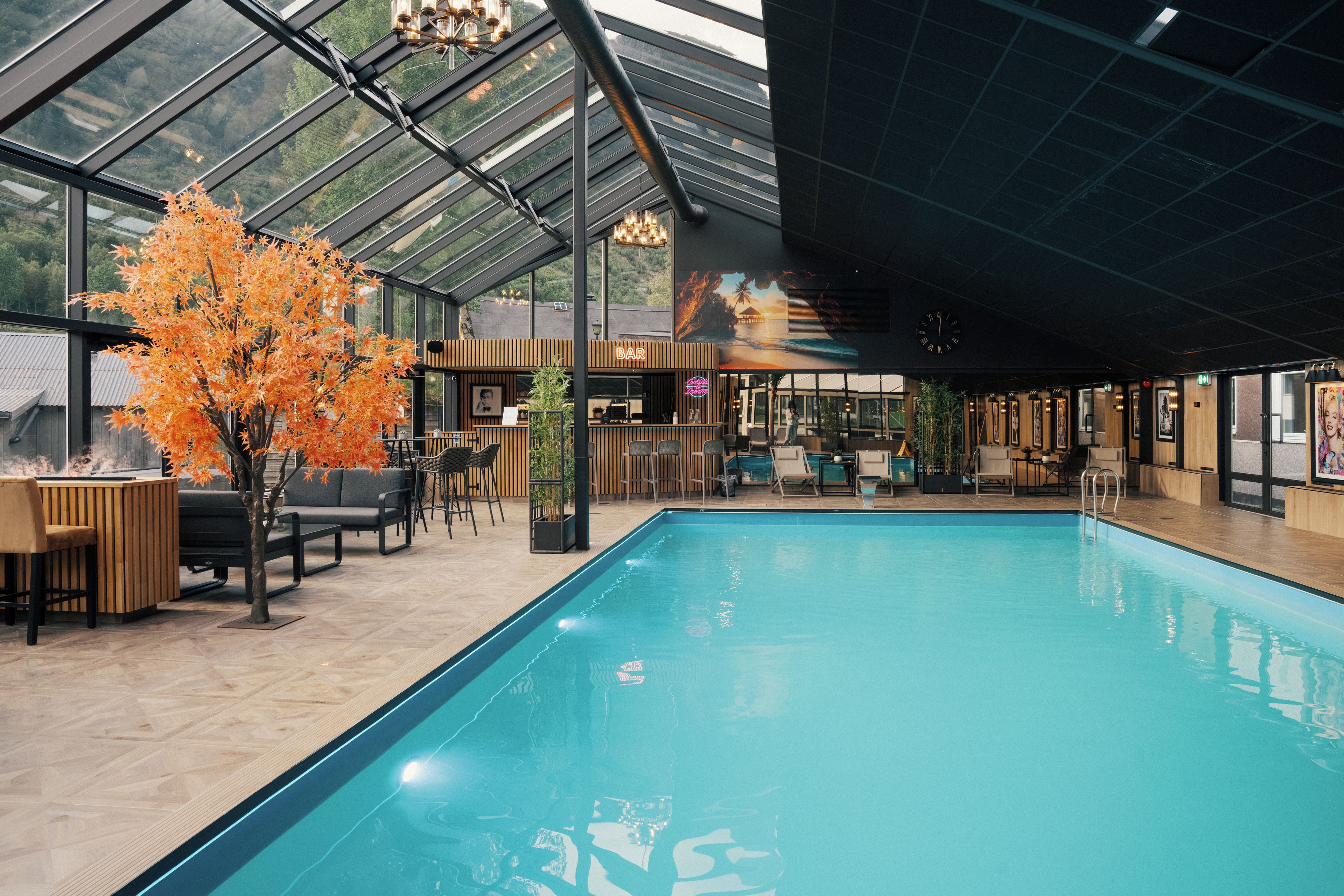 Una piscina interior con techo de cristal, asientos de madera y zona de bar.