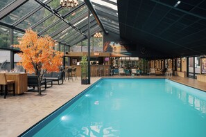 An indoor swimming pool with a glass ceiling, wooden seating, and a bar area. - Grand Hotel Skei - Unike Hoteller (Sunnfjord)