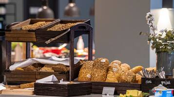 A bakery display with various breads and pastries, a sign indicating 'Dagens Brod', and a vase with flowers.