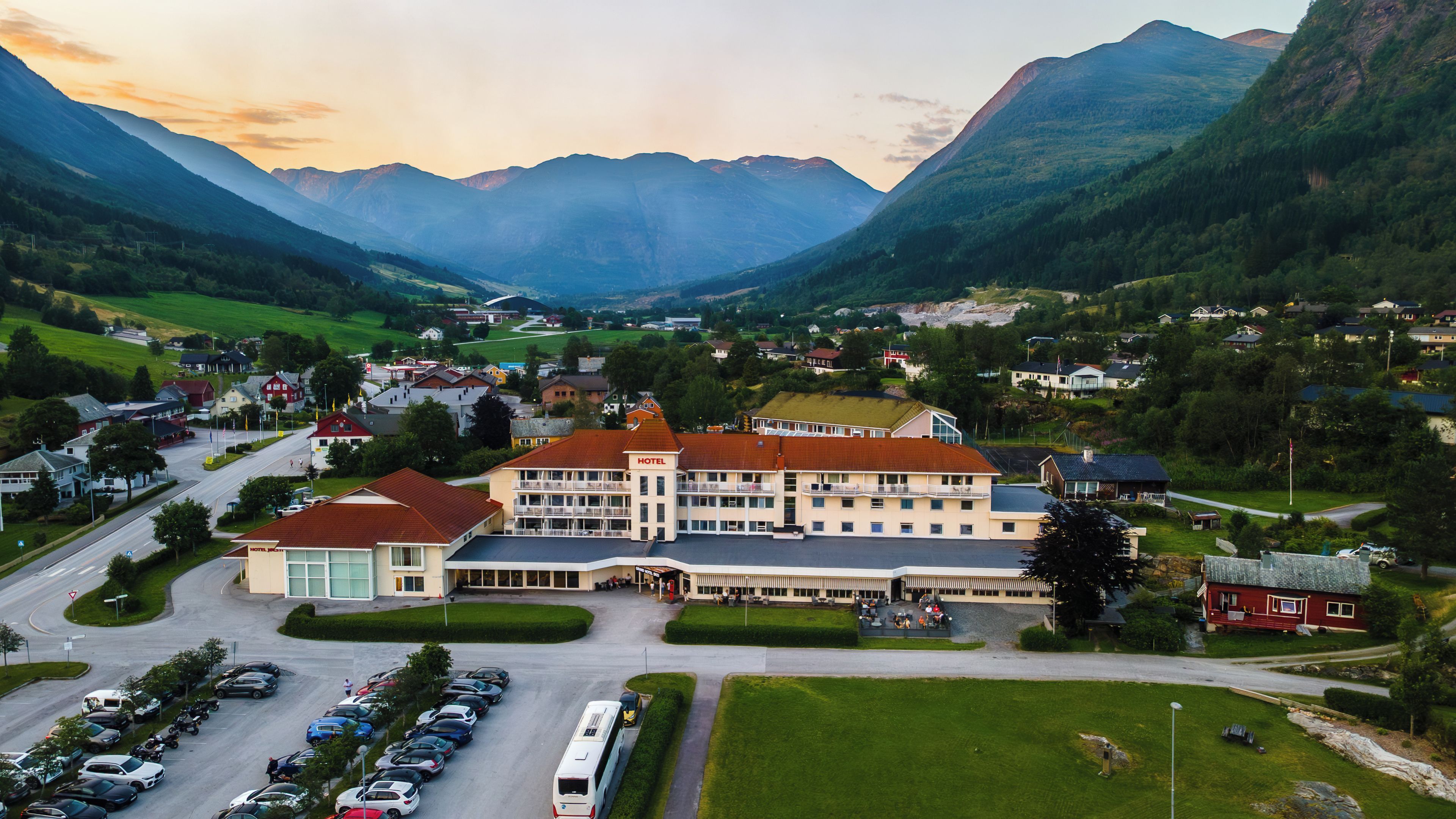A hotel with a large building, a parking lot, and a mountainous backdrop.