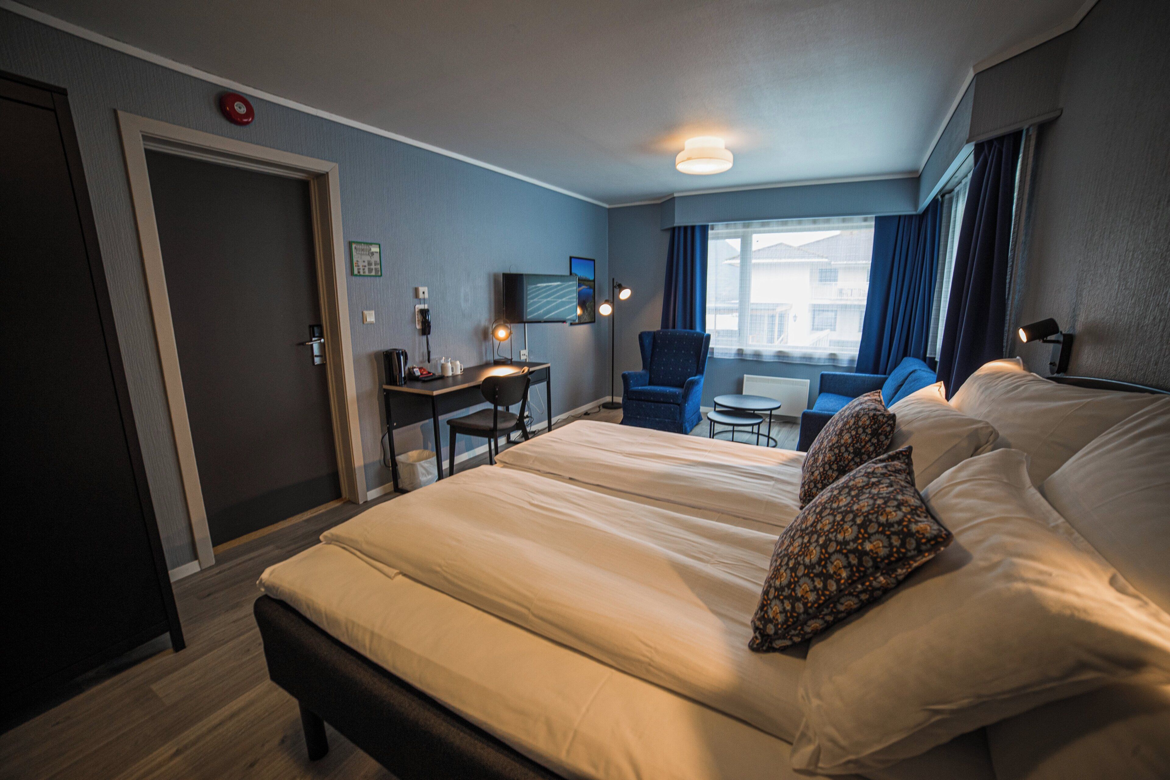 A hotel room with a large bed, a desk, a chair, and a TV.