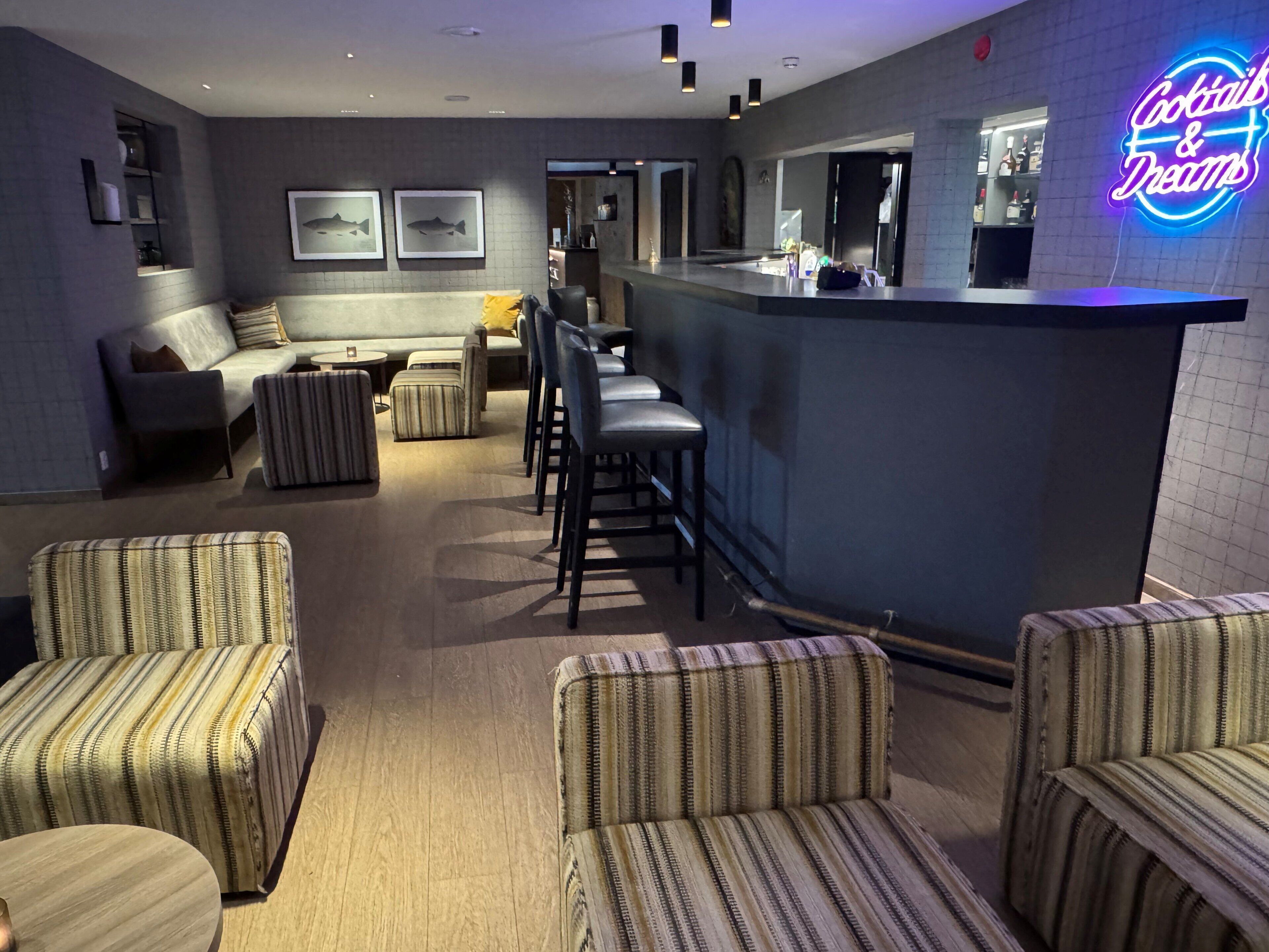 Un vestíbulo de hotel con sillones a rayas, una zona de bar y arte de pared con peces enmarcados.
