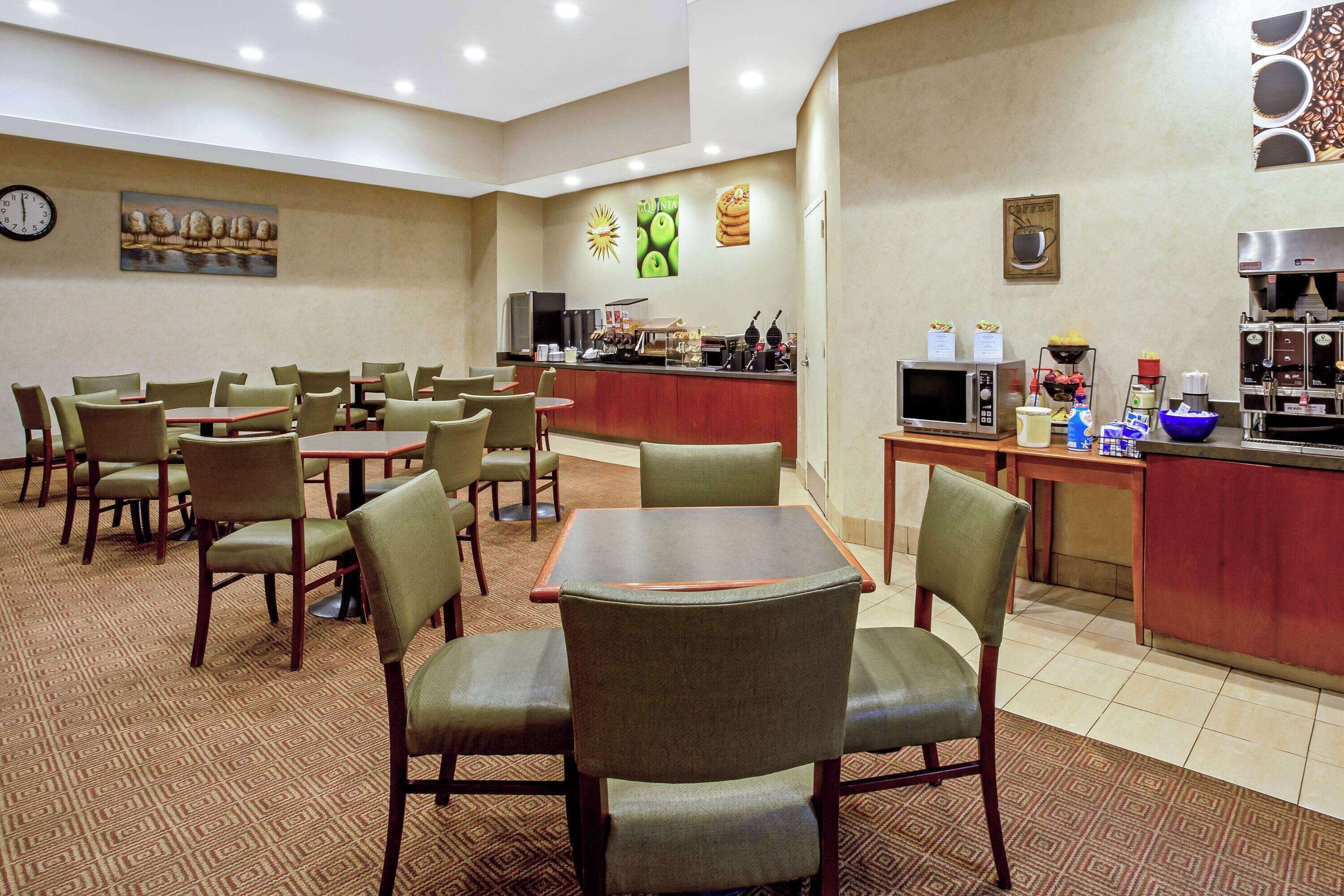 Een hotelrestaurant met meerdere tafels en stoelen, een koffiehoek en een klok aan de muur.