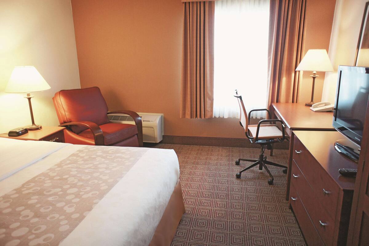 A hotel room with a bed, a desk with a lamp, a chair, a television, and a dresser.