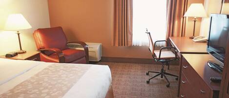 A hotel room with a bed, a desk with a lamp, a chair, a television, and a dresser.