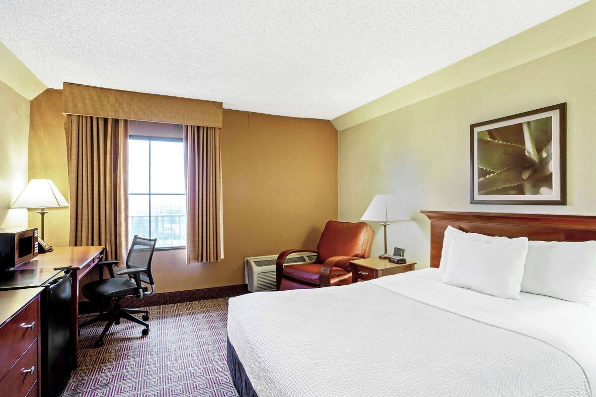 A hotel room with a large bed, a desk with a chair, a lamp, and a framed picture on the wall.