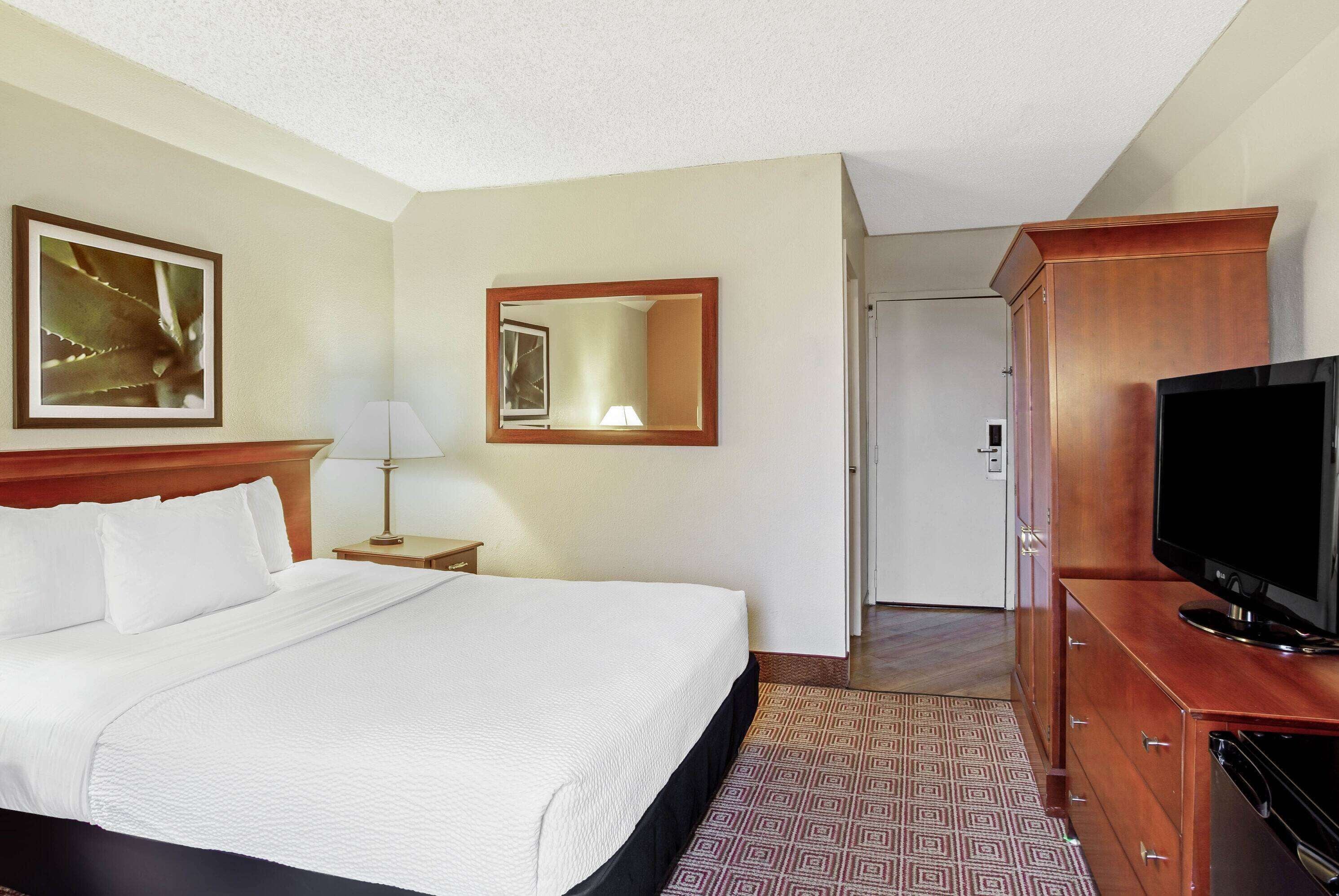 A hotel room with a large bed, a TV, a wooden dresser, a mirror, and a framed picture on the wall.