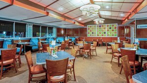 Ein Restaurant mit Sitzgelegenheiten in Form von Boxen und Tischen, einer Wand mit Muster und einer Decke mit freiliegenden Balken und Lampen.