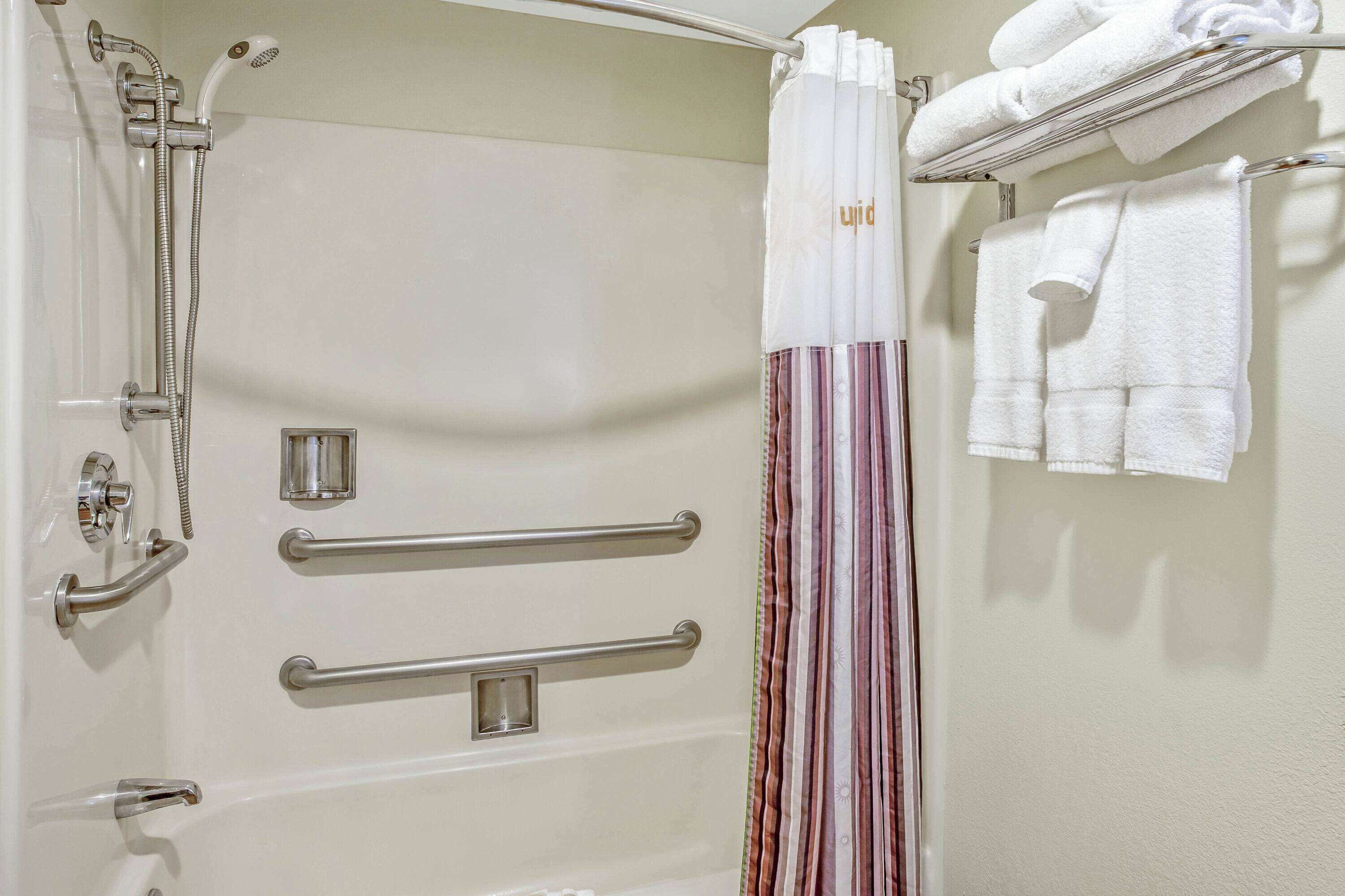 Une salle de bain équipée d’une douche, de barres d’appui, d’un porte-serviettes et d’un rideau de douche à rayures.
