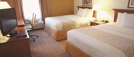 A hotel room with two beds, a desk with a television, a chair, and a window with curtains.