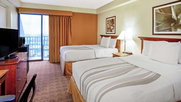 Ein Hotelzimmer mit zwei Betten, einem Fernseher, einem Schreibtisch und Blick auf die Stadt durch ein großes Fenster.