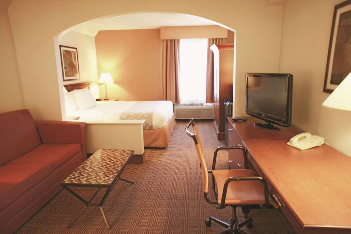 A hotel room with a bed, a desk with a TV, a sofa, a small table, and a chair.