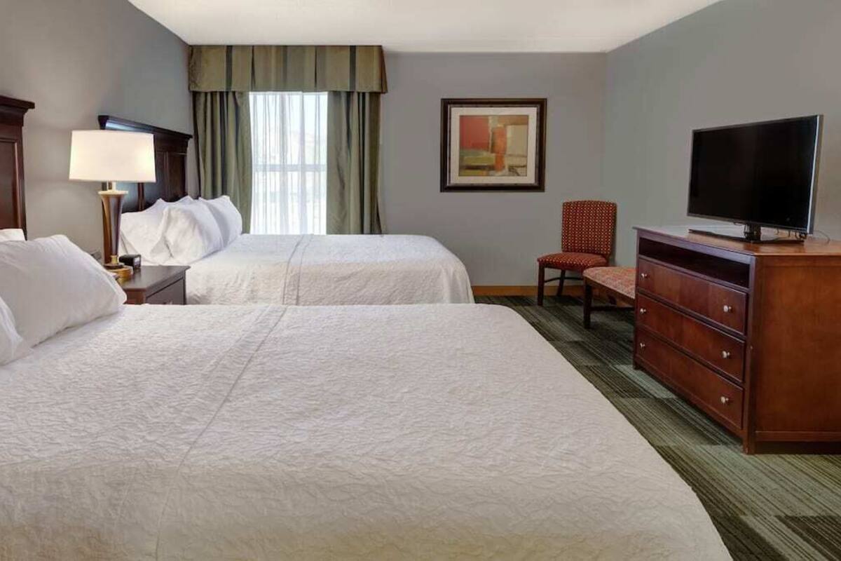 Una habitación de hotel con dos camas, televisión, escritorio, silla y cómoda.