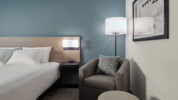A hotel room with a bed, a nightstand, a lamp, a chair, and a rug.