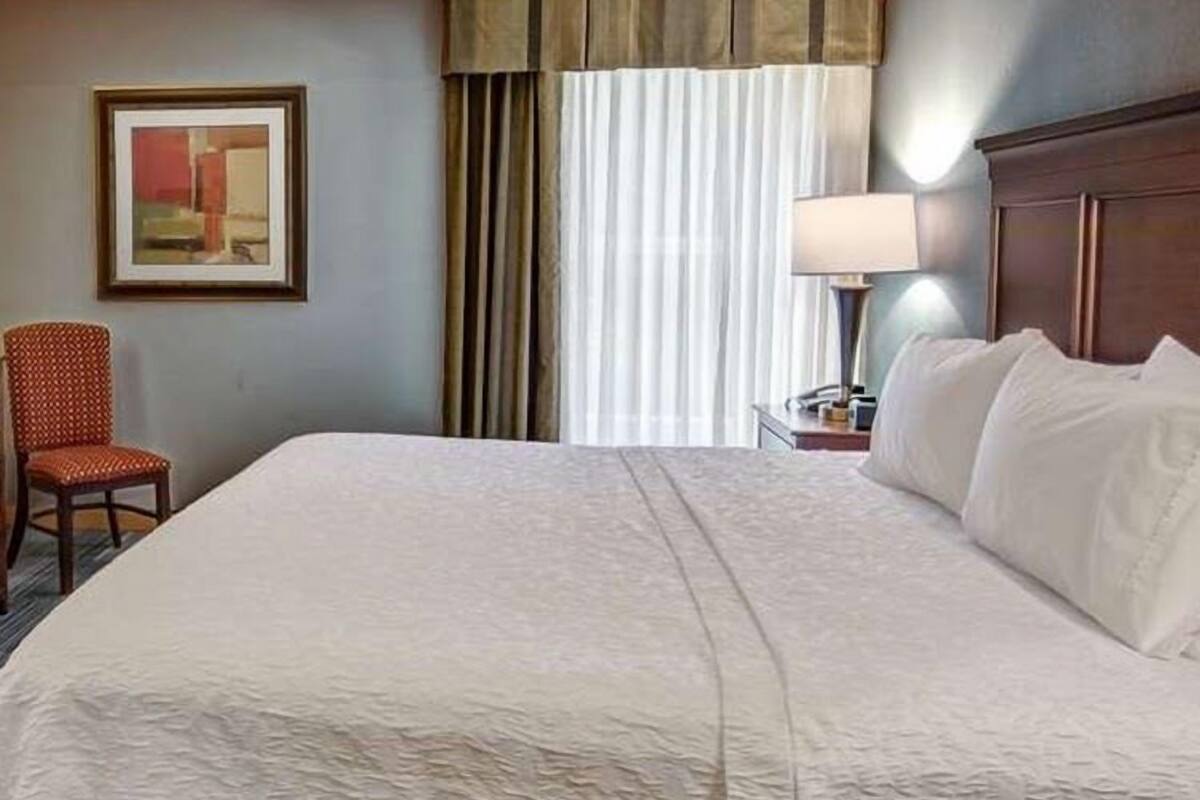 Habitación de hotel con una cama grande, una silla, una lámpara y un cuadro en la pared.