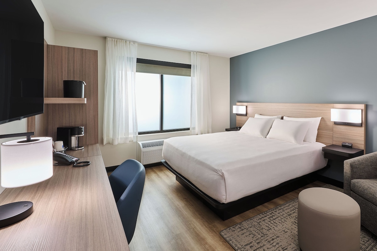 Habitación de hotel con cama, mesitas de noche, escritorio con lámpara, silla, sofá y televisor.