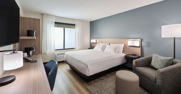 Habitación de hotel con cama, mesitas de noche, escritorio con lámpara, silla, sofá y televisor.
