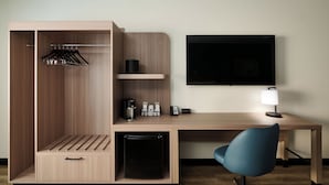 Een compacte hotelkamer met een bureau, stoel, kitchenette en een kledingkast met hangende kleding.
