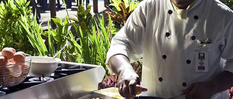 Un chef preparando comida al aire libre, con una parrilla y varios ingredientes a la vista.