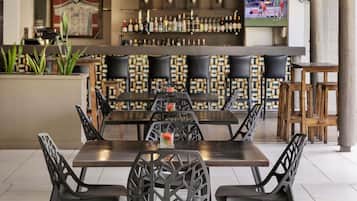 Un restaurante con una mesa larga, sillas negras, una zona de bar con botellas y una pantalla de televisión.
