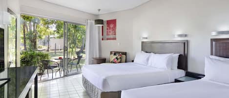 A hotel room with two beds, a desk, and a view of a garden.