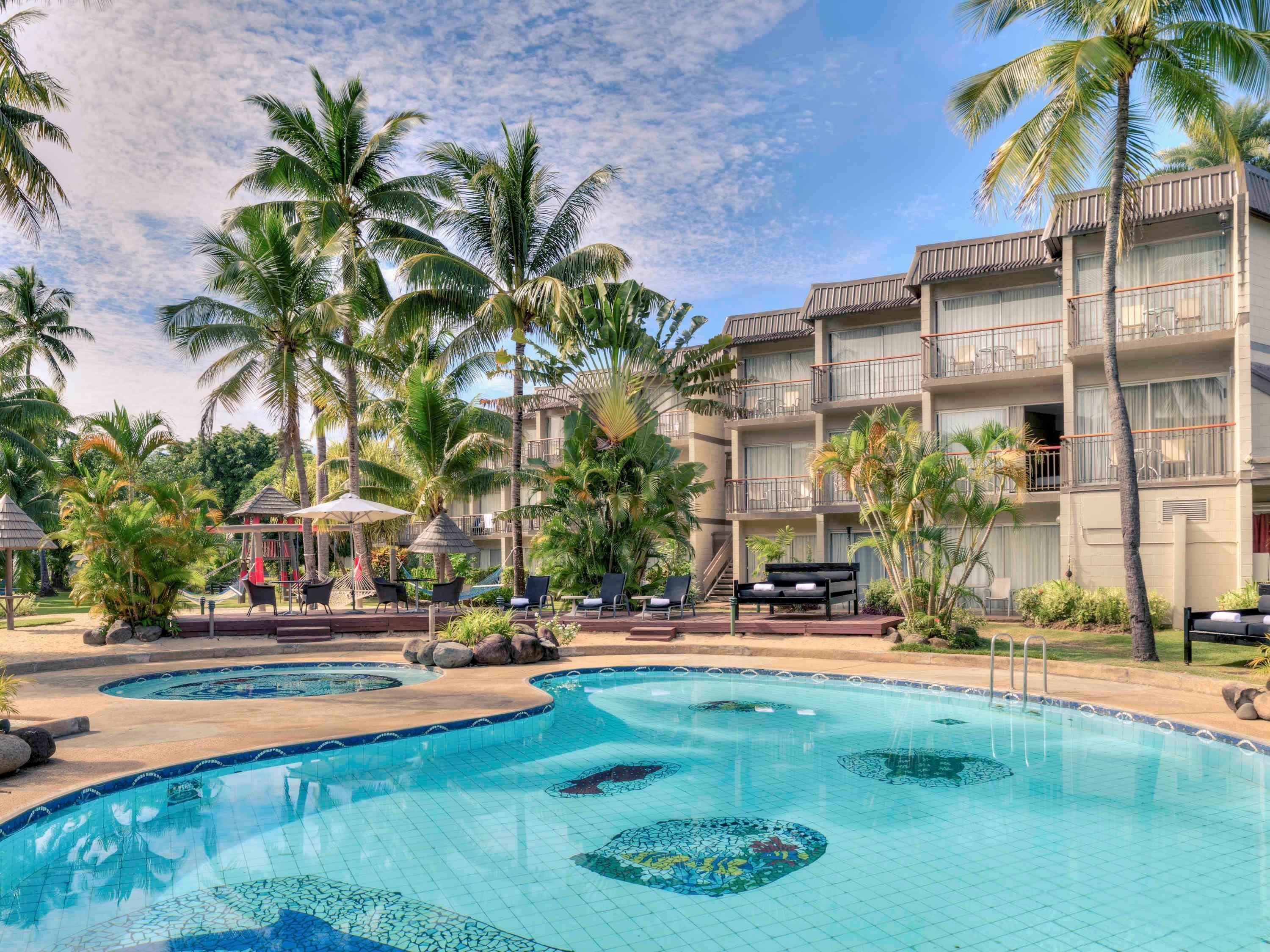 Un resort con piscina, palme e un edificio con balconi.
