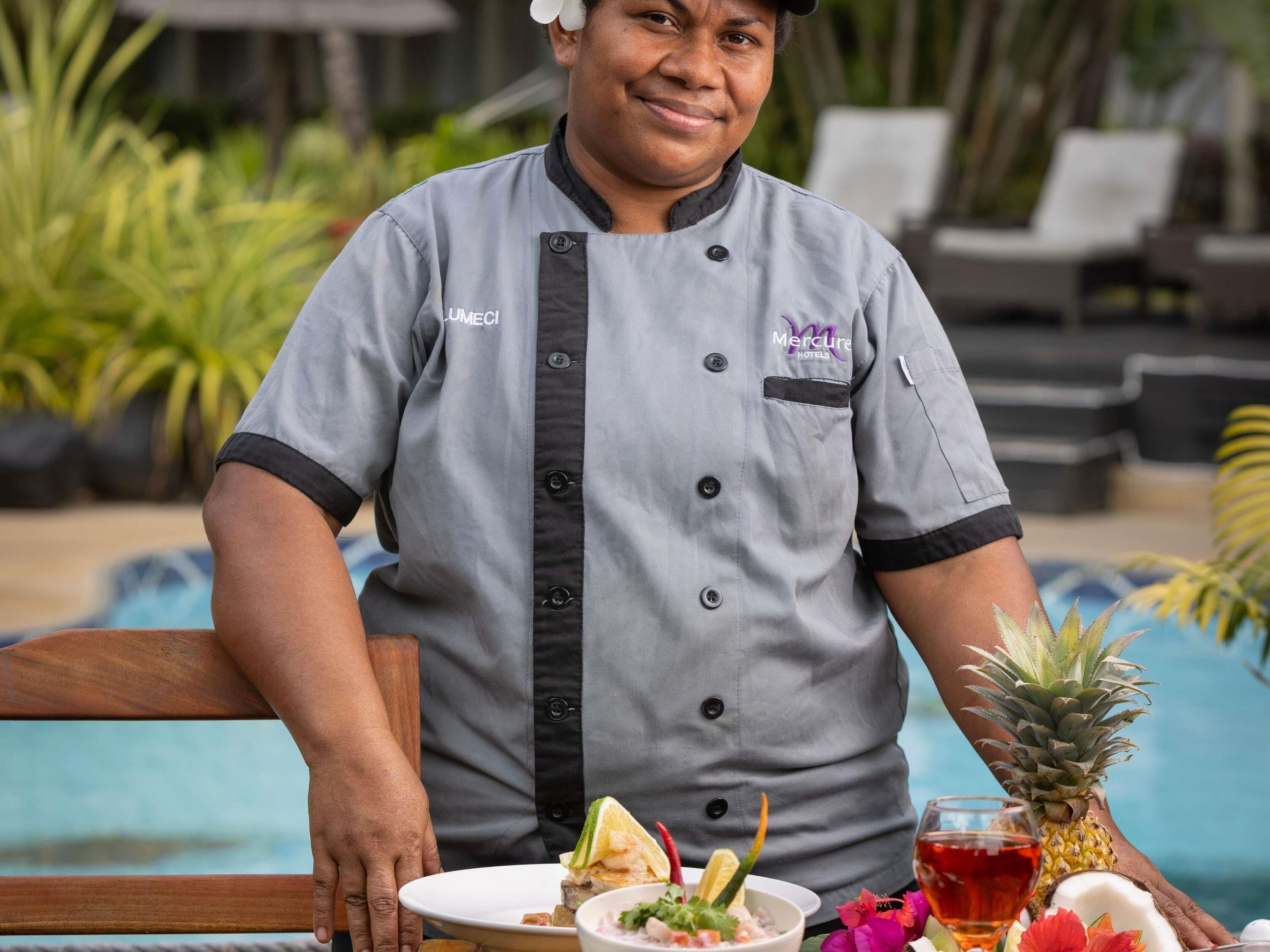 A person seated at a table with a plate of food, a pineapple, and a glass of red beverage.