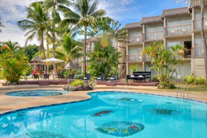 Un hotel con piscina, palmeras y zonas de estar al aire libre.