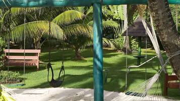A hammock swing, a wooden bench, and a small structure in a lush garden.
