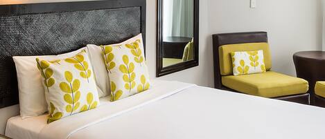 Una habitación de hotel con una cama grande, una silla, una mesita y un espejo en la pared.