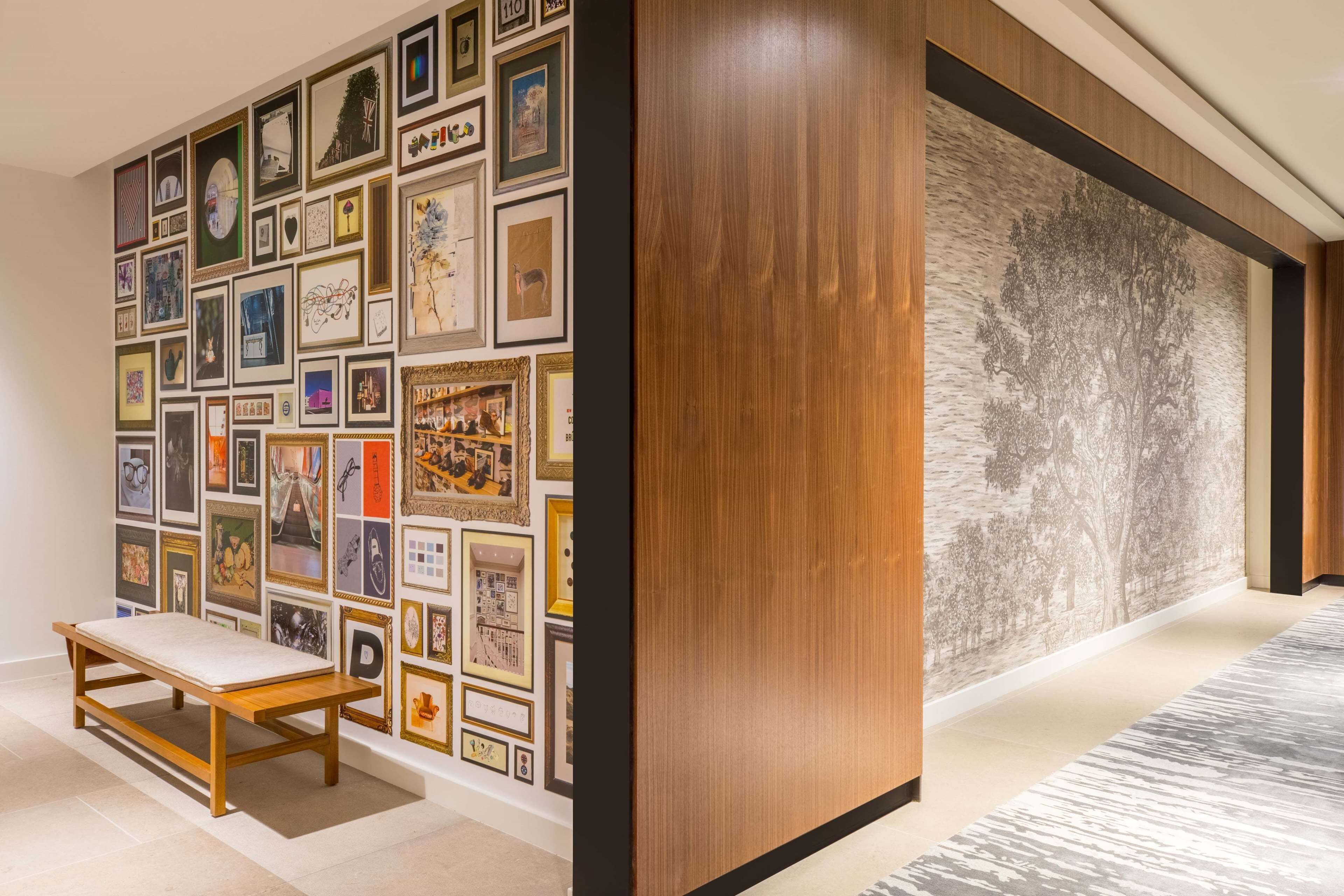 A hallway with a wooden bench, a wall decorated with framed pictures, and a large tree mural.