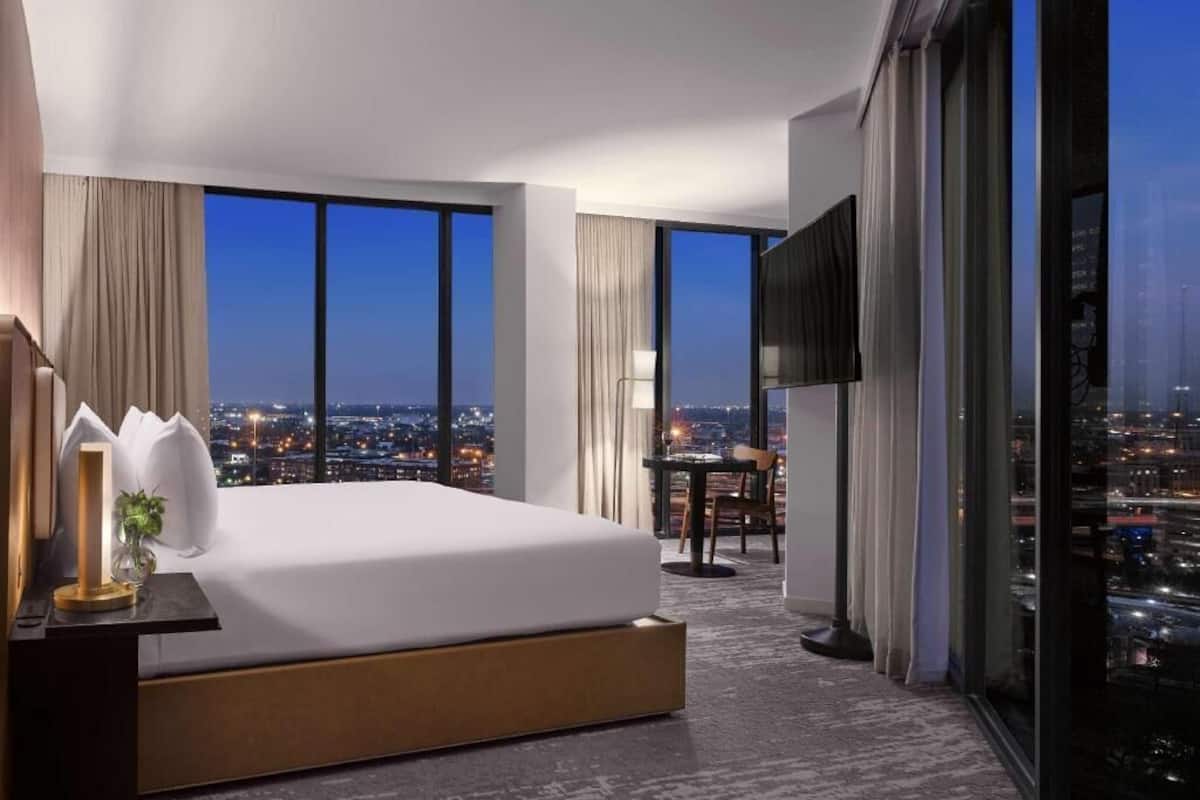 A modern hotel room with a large bed, a desk, and a TV.
