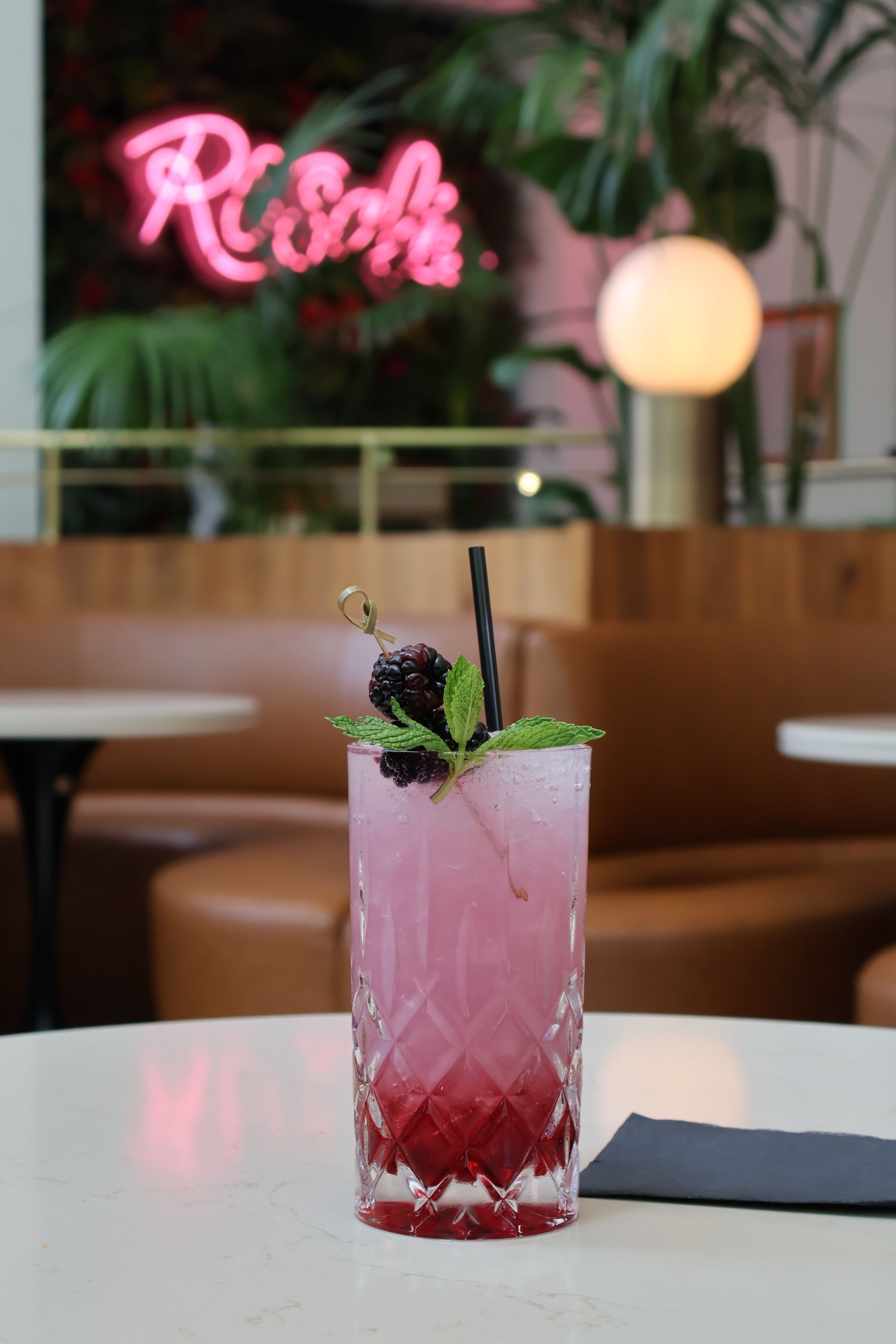 Ein pinkes Getränk mit Brombeerdurchschlag auf einem Tisch in einem Restaurant, im Hintergrund ein Neonlicht.