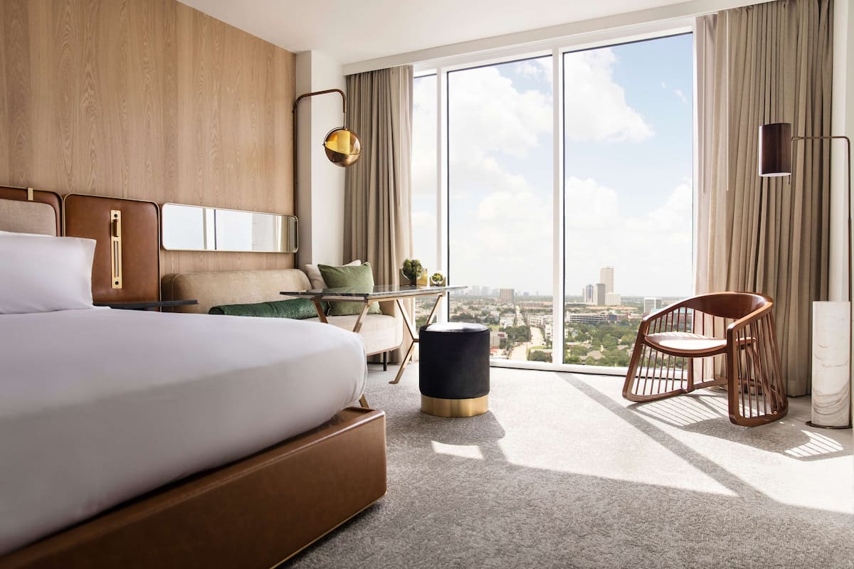 A modern hotel room with a large bed, a desk, a chair, and a view of the city.
