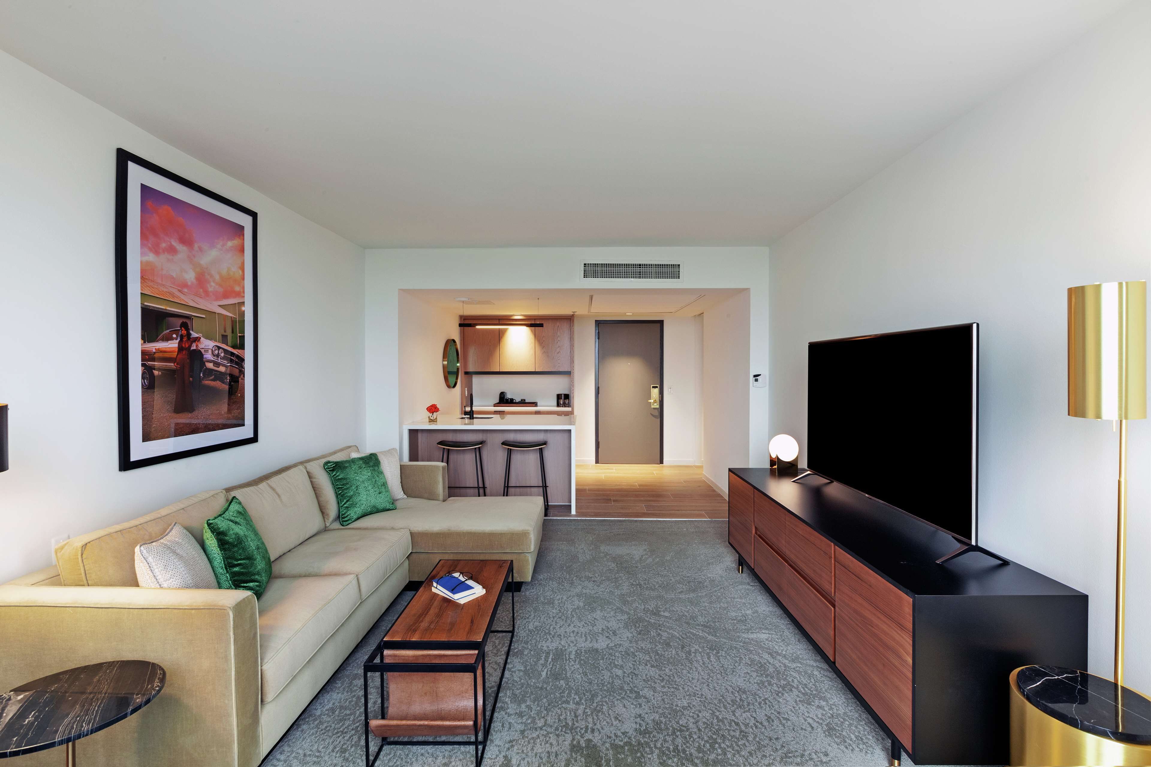 A modern living room with a sofa, coffee table, TV, and a kitchen area in the background.