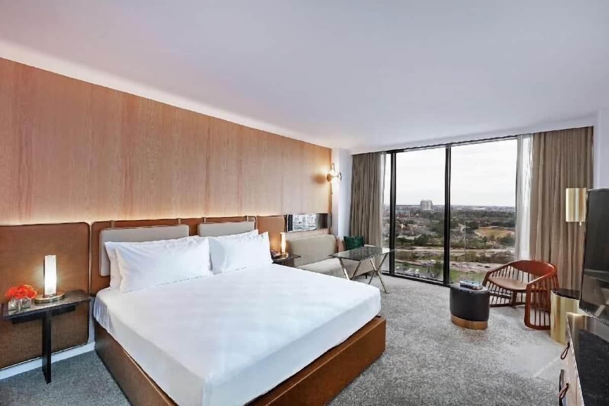 A hotel room with a large bed, a sofa, a TV, and a view of the city.