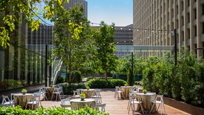 Une terrasse extérieure avec des tables et des chaises rondes, entourée de verdure et avec des bâtiments modernes en arrière-plan.