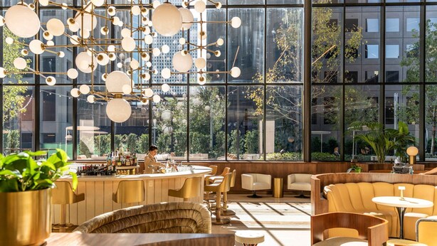 Un intérieur moderne avec un bar, des espaces pour s’asseoir et de grandes fenêtres offrant une vue sur la ville.