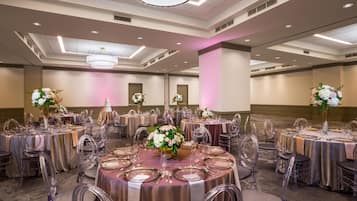 A banquet hall with round tables set for dining, clear chairs, and floral centerpieces.