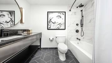 A modern bathroom with a black and white tiled floor, a white toilet, a bathtub, and two framed black and white photographs on the wall.