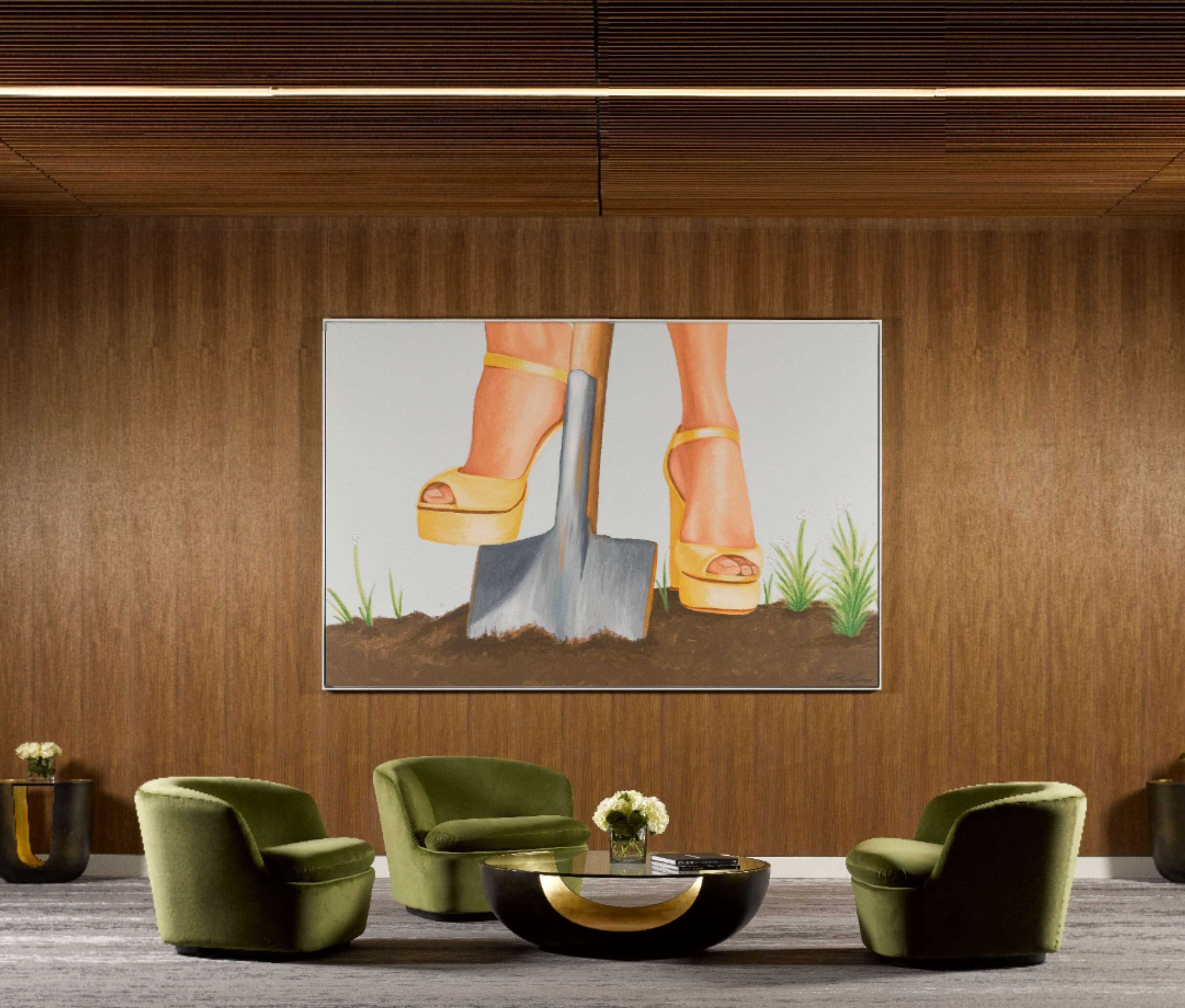 A room with a large painting of feet in yellow high heels shoveling soil, two green armchairs, and a black coffee table with a vase of flowers.