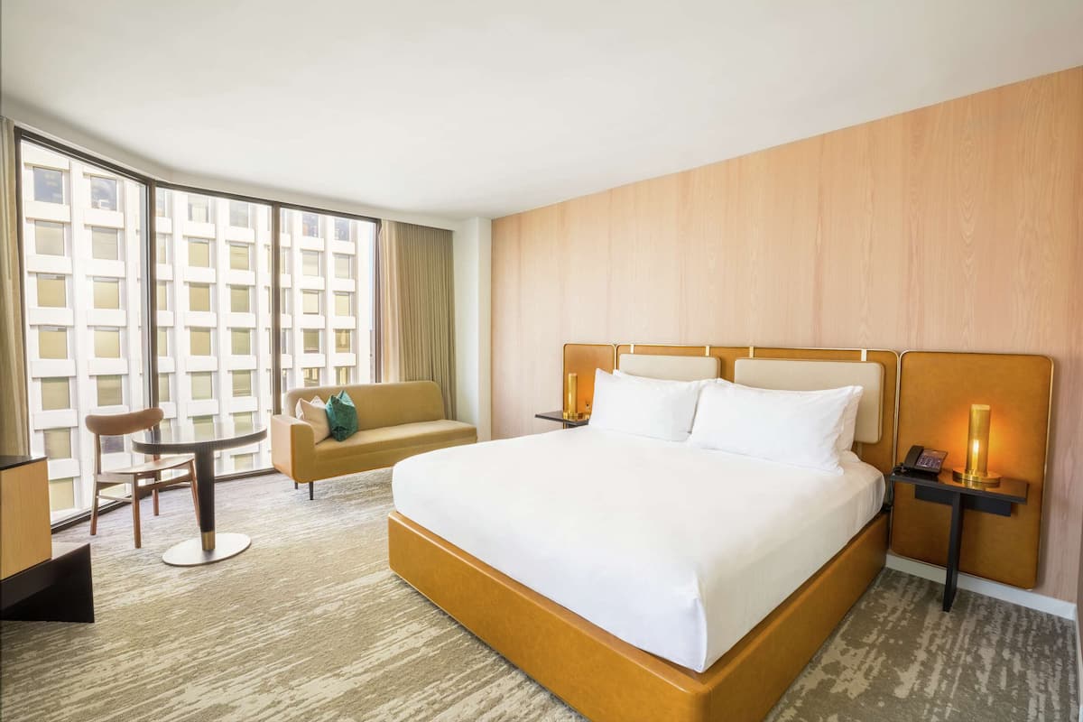 A hotel room with a large bed, a sofa, a small table, and a nightstand with a lamp.